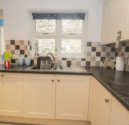A kitchen countertop with a sink under a window and cabinets at Ty Potiwr in Conwy