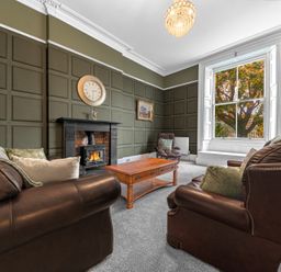 A living room with leather sofas a wooden coffee table fireplace and a large window at 8 Corkickle Whitehaven
