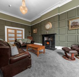A living room with leather sofas a wooden coffee table a fireplace a clock on the wall and framed paintings at 8 Corkickle in Whitehaven