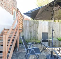 A wooden staircase leading to a door beside a patio area with black chairs and a glass table with a black umbrella at Crab Corner in Wells-Next-The-Sea