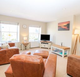 A living room with brown leather sofas a television on a stand and a floor lamp at Crab Corner in Wells-Next-The-Sea