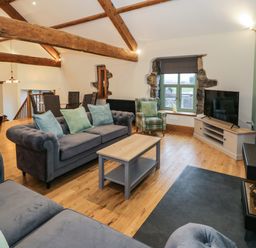 A living room with blue sofas a coffee table a plaid armchair a television on a cabinet a pool table and wooden beams at The Barn by Lyons in Talybont near Barmouth