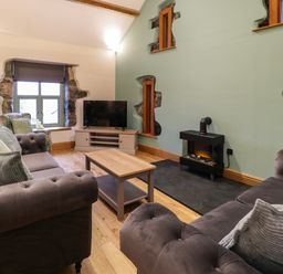 A living room with two sofas a coffee table a TV and a stove at The Barn by Lyons Talybont near Barmouth