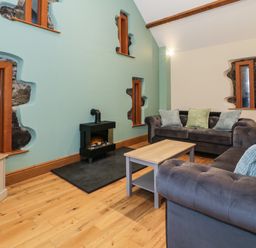 A living room with a wooden floor sofas cushions a small fireplace and irregular windows at The Barn by Lyons Talybont near Barmouth