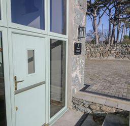 A pale green door with glass panels next to a stone wall and paved driveway at The Barn by Lyons in Talybont near Barmouth