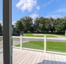 A balcony with glass railing overlooking a green lawn trees and mobile homes at 7 The Oaks in Long Preston near Hellifield
