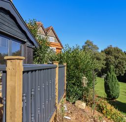 A wooden balcony railing with garden and greenery in the background at Sir George Baker Cabin in Uplyme