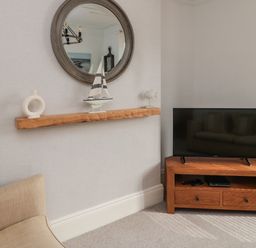 A corner of a living room with a wooden TV stand holding a television next to a beige armchair and a wall shelf with decorative items at 18 Acklington Road in Amble