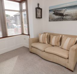 A beige sofa with three cushions under a boat painting next to a window with blinds at 18 Acklington Road in Amble