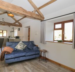 A living area with a blue sofa and wooden beams on the ceiling near a kitchen and dining table at Keepers Barn in Bromyard