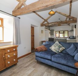 A living room with wooden beams a blue sofa and a wooden cabinet at Keepers Barn in Bromyard