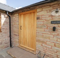 An entrance with a wooden door and stone wall at Keepers Barn in Bromyard