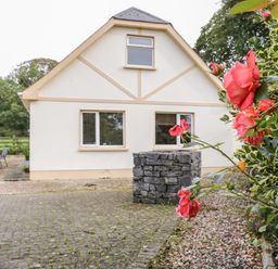 A house with beige walls and three windows with a stone structure and red flowers in front at Shore Road in Culdaff County Donegal