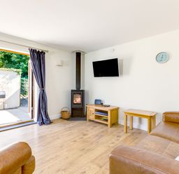 A living room with brown leather sofas a wood stove and TV mounted on the wall at Chy Pol in St Minver