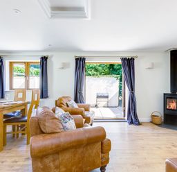 A living room with leather sofas wooden dining table wood stove and open doors to a patio at Chy Pol in St Minver