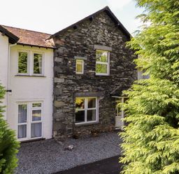 An exterior view of a house with stone and white walls surrounded by trees at Silver How in Ambleside