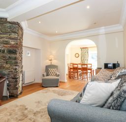 A living room with a stone fireplace chairs and a dining table visible through an archway at Silver How in Ambleside