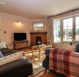 A living room with sofas a coffee table a fireplace and large windows at Rookery Cottage in Kelsale near Saxmundham