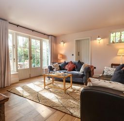 A living room with two sofas a glass coffee table and large windows at Rookery Cottage in Kelsale near Saxmundham