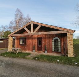 A wooden cabin with a picnic table outside on a lawn near a gravel driveway at Matfen in Longframlington