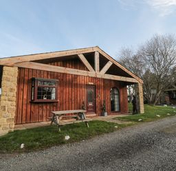 A wooden cabin with stone pillars and a picnic bench outside at Matfen in Longframlington