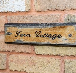A wooden sign with the text Fern Cottage mounted on a brick wall at Fern Cottage in St Brides-Super-Ely