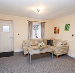 A living room with a striped corner sofa cushions a coffee table flowers on the table paintings on the wall at Fern Cottage in St Brides-Super-Ely