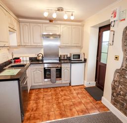 A kitchen with tiled floor stone wall cabinets oven sink microwave and a door at Fern Cottage in St Brides-Super-Ely