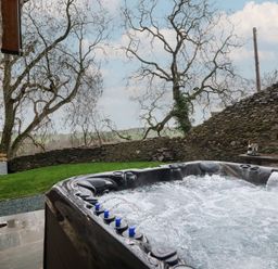 A hot tub with a view of a stone wall and trees at Godre'r Gyrn, Plas Moelfre Hall Barns, Oswestry