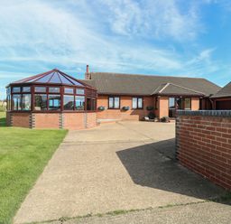 A driveway leading to a brick house with a glass conservatory and a double garage at Beach Haven in Happisburgh East Anglia