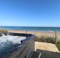 A hot tub on a patio overlooking a sandy beach and the sea at Beach Haven in Happisburgh East Anglia
