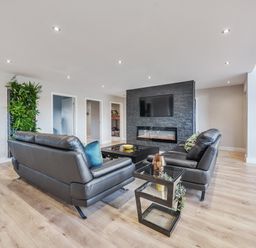 A living room with black leather sofas a glass side table a wall-mounted tv and an electric fireplace at Micklemore Lakes and Lodges in North Thoresby