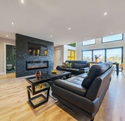 A living room with black leather sofas a black stone fireplace and a dining table near large windows at Micklemore Lakes and Lodges in North Thoresby