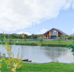 A wooden house near a lake with trees and grass around at Micklemore Lakes and Lodges in North Thoresby