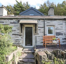Stone cottage entrance with a wooden bench and plants at 4 Ty Person in Braichmelyn near Bethesda