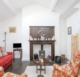 A living room with a fireplace a red sofa armchairs and a small table at 4 Ty Person in Braichmelyn near Bethesda