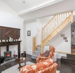 A living room with orange patterned armchairs a wooden staircase and a fireplace with decorative items at 4 Ty Person in Braichmelyn near Bethesda
