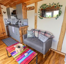 A small living area with a gray sofa, colorful coffee table, and kitchenette with gray cabinets and wooden accents at Moel Y Parc in Bryniau Clwyd near Denbigh