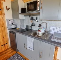 A kitchen with grey cabinets a sink a microwave and utensils at Moel Y Parc in Bryniau Clwyd near Denbigh