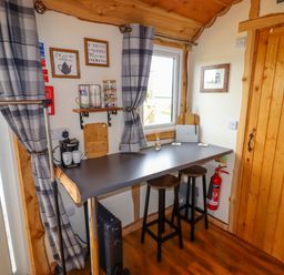 A small dining area with a counter table and two stools near a wooden door and window at Moel Y Parc in Bryniau Clwyd near Denbigh
