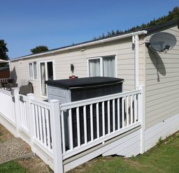 An exterior view of a beige mobile home with white railing around a porch and a satellite dish on the side at 116 Woodpecker Lodge in Gilfachrheda near Llanarth