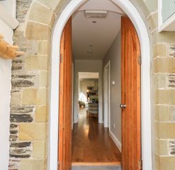 A stone arched doorway with wooden double doors opening to a hallway with hardwood flooring leading to a living area at Upper Vestry in Llangrannog