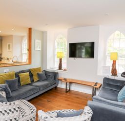 A living room with sofas, patterned armchairs, a wall-mounted TV, wooden bench, and lamps by windows at Upper Vestry in Llangrannog