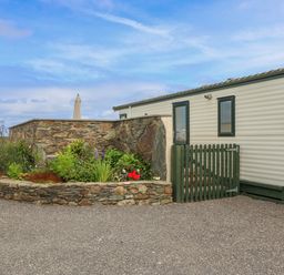 An exterior view of a mobile home with green windows and a small garden with plants and flowers at Cae Gog Near Cemaes Bay