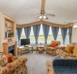 A living room with floral sofas a television on a wooden table blue curtains and a ceiling fan at Cae Gog Near Cemaes Bay