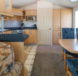 A kitchen and dining area with wooden cabinets a stove and blue patterned chairs at Cae Carreg in Cemaes Bay