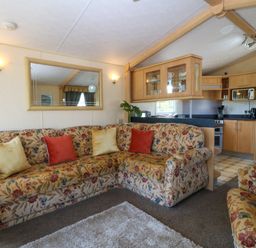 A living room with floral patterned sofas and cushions next to a kitchen with wooden cabinets at Cae Carreg in Cemaes Bay