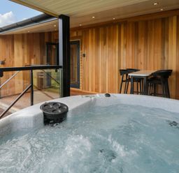 An outdoor hot tub on a wooden deck with a table and four chairs at Betsi Lodge 1 in Llanelidan near Corwen