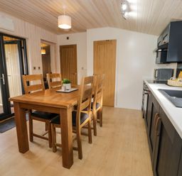 A kitchen and dining area with a wooden table and chairs next to black cabinets and a sink at Betsi Lodge 1 in Llanelidan near Corwen