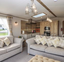 A living room with sofas and cushions next to a kitchen with wooden cabinets and dining area at Hazel Lodge in Teigngrace near Newton Abbot